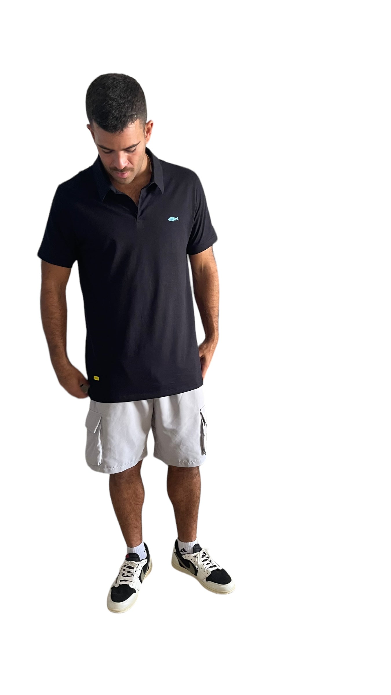 100% pima cotton polo shirt with a minimalist blue fish emblem on the chest, worn by a man styled with black cargo shorts and sporty black-and-white sneakers. The polo features a structured collar and short sleeves, offering a crisp yet relaxed everyday look.
Polo blanco de algodón 100% con un pequeño emblema de pez azul en el pecho, usado por un hombre con pantalones cortos tipo cargo negros y zapatillas deportivas en blanco y negro. Camisa tipo polo de corte clásico con cuello estructurado y mangas
