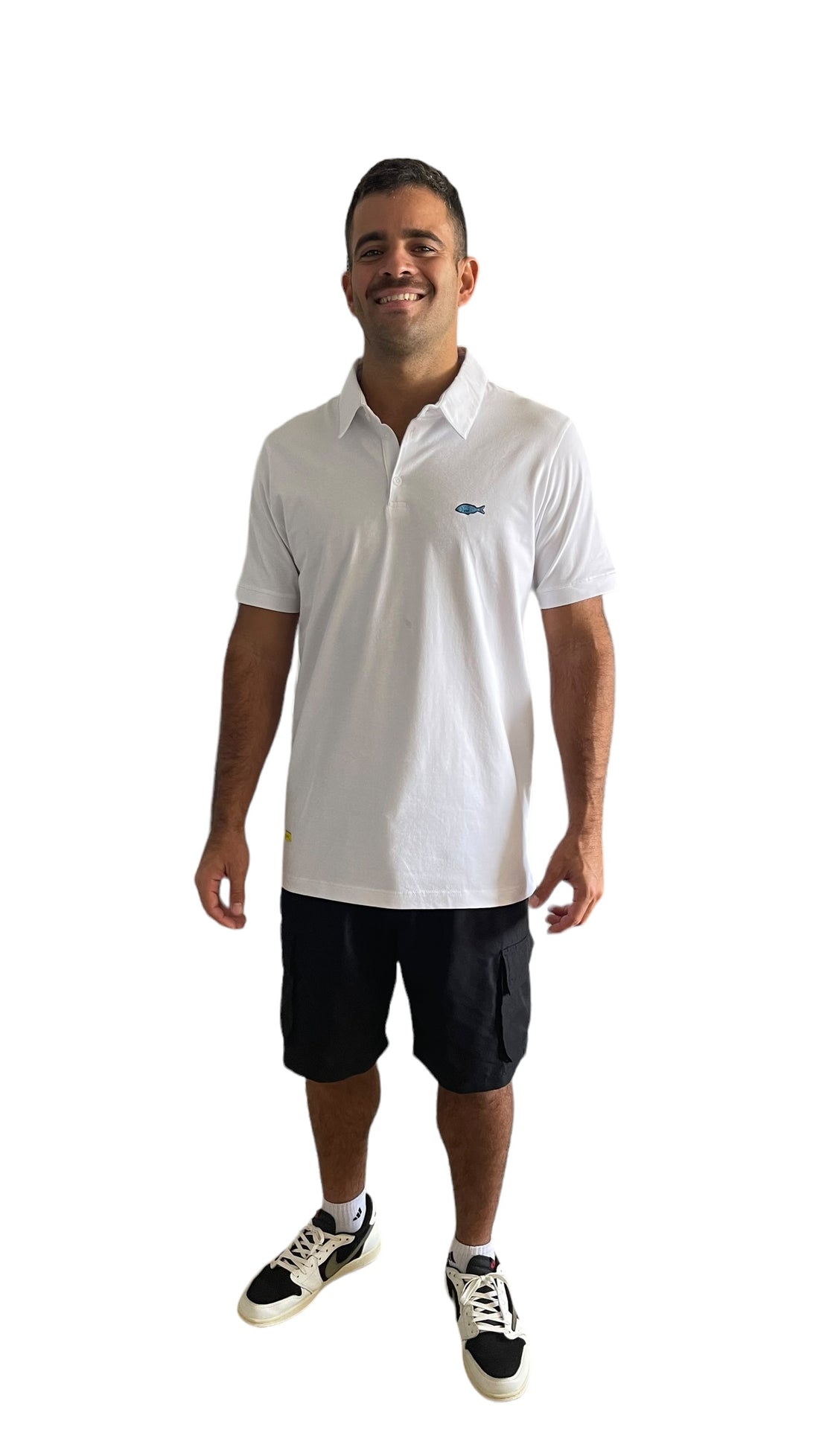 Polo de algodón  Pima 100% con un pequeño emblema de pez azul en el pecho, usado por un hombre con pantalones cortos tipo cargo negros y zapatillas deportivas en blanca.Camisa tipo polo de corte clásico con cuello estructurado y mangas cortas, ideal para un look casual y fresco.
White 100% Pima cotton polo shirt with a minimalist blue fish emblem on the chest, worn by a man styled with black cargo shorts and sporty black-and-white sneakers. The polo features a structured collar and short sleeves,